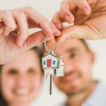 A smiling couple holds a house-shaped key, symbolizing their new home purchase.