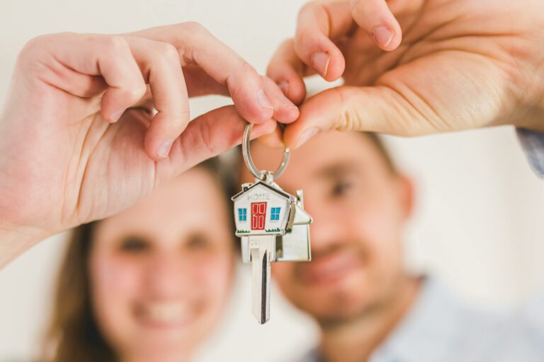 A smiling couple holds a house-shaped key, symbolizing their new home purchase.